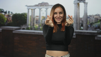 Obraz premium Young woman making twin finger heart gestures showing midriff at building columns and terrace; playful confidence.