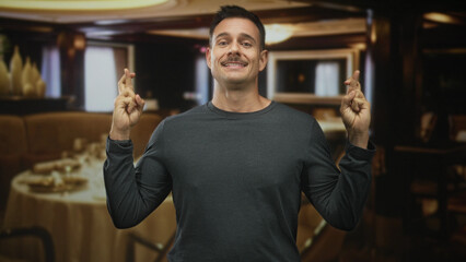 Obraz premium Man with moustache pressing hands together in prayer at a restaurant table inside a building; hopeful plea.