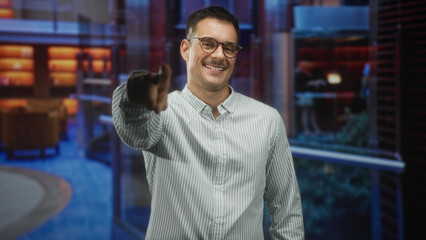 Fototapeta premium Man with moustache pointing finger at camera in modern building lobby wearing glasses and striped shirt; friendly invitation.
