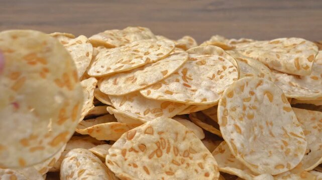 Multiple hands picking up pieces of crispy tempeh chips from a pile