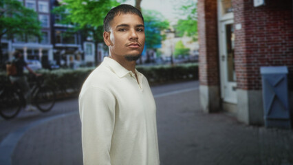 Obraz premium Man walking in profile with face visible past a brick building on street wearing a white sweater; calm reflection.