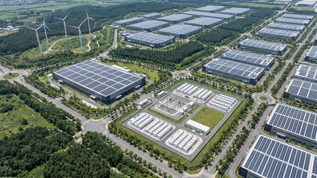 Aerial view of large sustainable industrial logistics park with solar panels on warehouse rooftops battery energy storage electrical substation and wind turbines clean technology eco concept