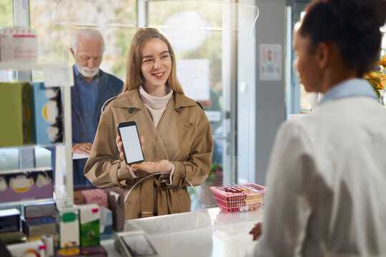 Smiling woman showing her prescription on smart phone to a pharmacist in a pharmacy