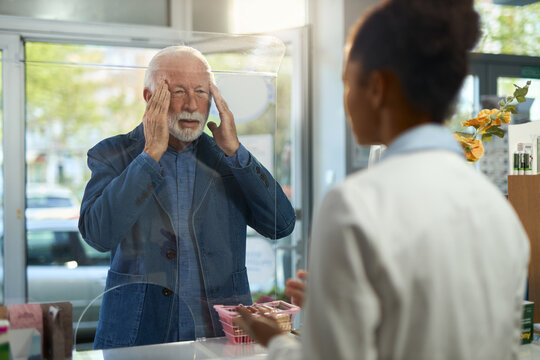 Displeased senior man with a headache buying a medicine in a pharmacy.