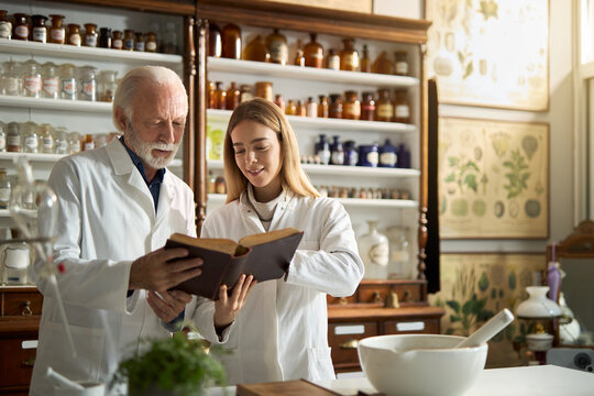 Happy student of science and her senior colleague reading an old medical book in a laboratory