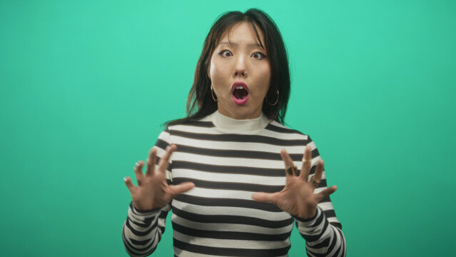 Woman with hands raised and fingers splayed making an expressive surprised face while speaking to camera in studio; surprise.