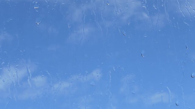 Raindrops sliding down glass window against soft blue blurred background