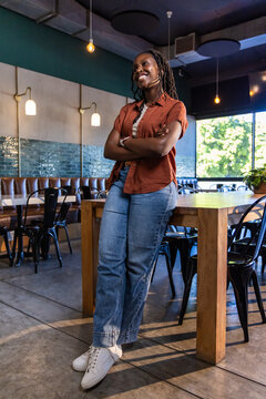 African American woman leaning against communal table in cafe, wearing rust shirt lavalier mic