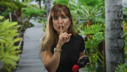 Fototapeta premium Woman holding a game controller and finger to lips for silence in forest; playful gentle secrecy hush.