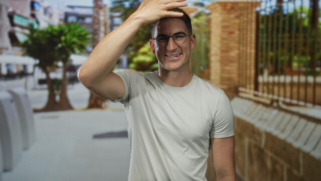 Man with hand covering face on a city street beside a brick wall and palm tree near railing; apology embarrassed.