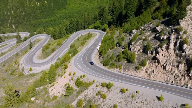 Panoramic Drone Shot Reveals Twisting Mountain Highway Amidst Lush Green Rocky Landscape During Summer