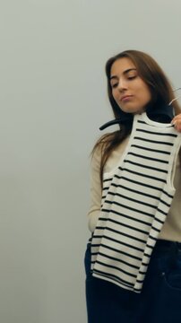 Summer fashion in fitting room. Light boutique setting with woman trying on striped summer top. Relaxed woman in boutique examines striped tank top for casual summer outfit selection