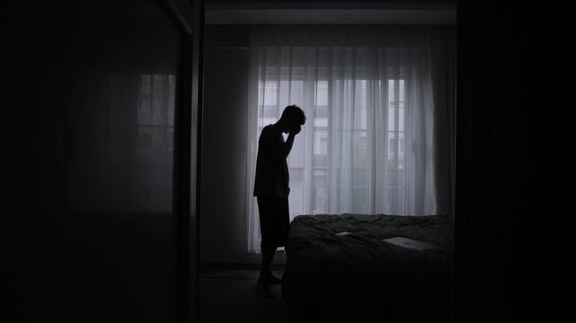 Stressed traveler standing in dark apartment doorway feeling homesick emotionally overwhelmed and exhausted from constant relocation and lonely temporary living