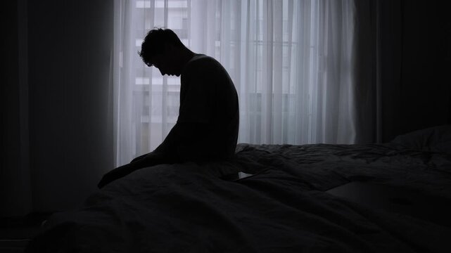 Lonely expat sitting on bed in temporary apartment feeling homesick emotionally exhausted and burned out from constant travel and unstable lifestyle