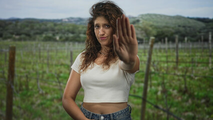 Obraz premium Woman raises palm to camera in forest showing stop gesture and stern expression, cropped midriff visible; defiance protection.