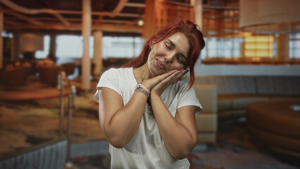 Fototapeta premium Young woman smiling and clapping hands then resting head on palms in restaurant lounge with warm lighting; joy relaxation.