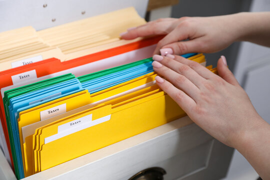 Tax. Woman looking through office folders in drawer of cabinet indoors, closeup