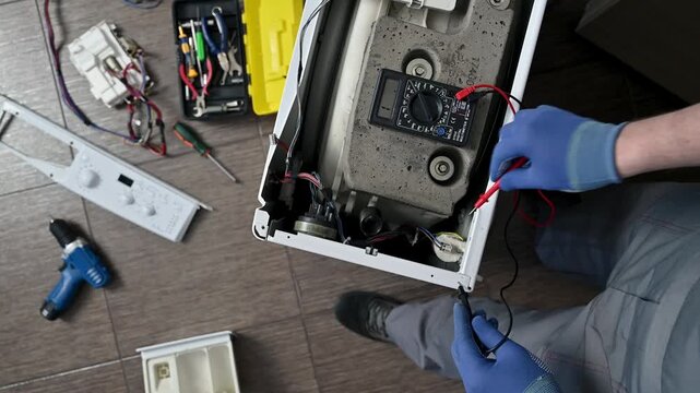 Top view a professional washing machine repair. A service engineer tests the integrity of the circuits and the functionality of capacitor.