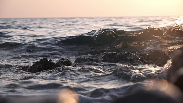 Wave and shore rock splashing at sunset, slow motion