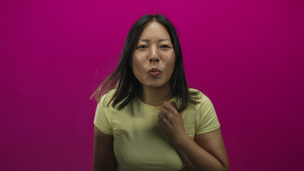 Fototapeta premium Young hispanic woman points index fingers forward toward camera in studio against magenta wall while wearing yellow t shirt; playful confidence.