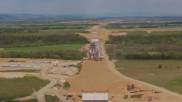 Impressive highway construction site with tall concrete bridge pillars and heavy machinery in the sweeping rural landscape towards Fagaras, slow aerial push in 4K
