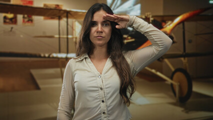 Woman salutes with hand to forehead inside museum building beside biplane exhibit  respect memory heritage. © Krakenimages.com