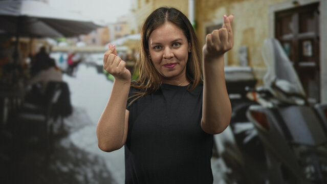 Woman making finger heart with fingers and hands while standing on a street terrace at a restaurant; playful affection.
