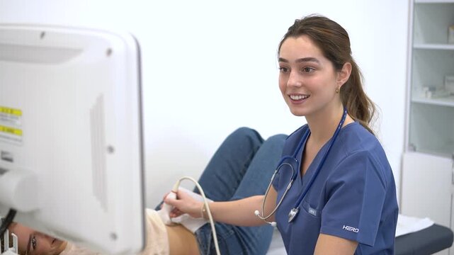 Happy female doctor smiling while performing ultrasound scan on patient in professional clinical lab. Healthcare specialist using sonogram machine for medical checkup and abdominal imaging test.