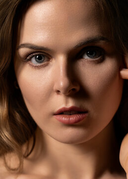 Woman's face close up featuring blue eyes, brown hair, lips, and skin texture
