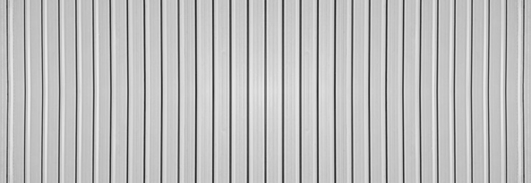 grey silver gray corrugated metal wall background texture with vertical lines and rivets. Clean industrial surface for construction or architectural backdrop. Frontal view with bright natural light.