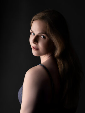 Young woman looking back over shoulder, side lighting highlighting her face on dark background