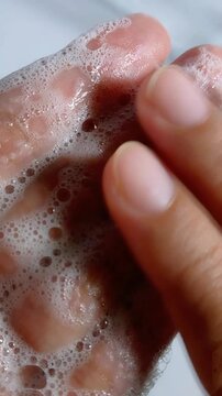 Gently rubbing soap foam bubbles on wet palm of hand. Close up view showing detailed wet skin texture and delicate foam bubbles. Skincare and cleansing concept.
