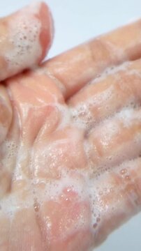 Close up of rubbing and spreading white foam on palm of hand. Detailed view of foamy texture and bubbles being massaged into skin. Skincare and cleansing product demonstration.