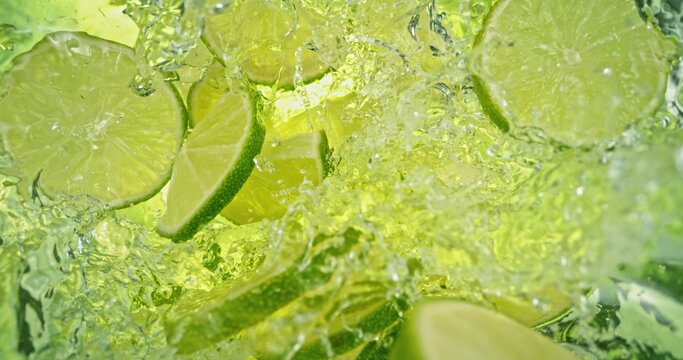 Fresh lime slices falling into sparkling water with bubbles and splashes. Bright green citrus macro photo, perfect for beverage, freshness, summer, cocktail and healthy lifestyle visuals.