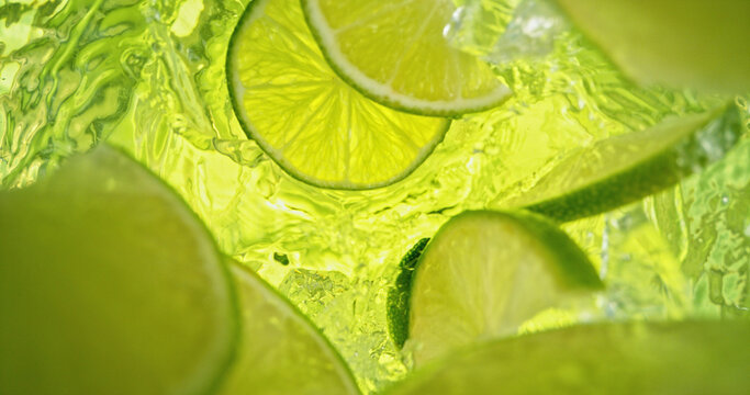 Fresh lime slices falling into sparkling water with bubbles and splashes. Bright green citrus macro photo, perfect for beverage, freshness, summer, cocktail and healthy lifestyle visuals.