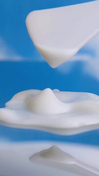 Scooping white cream with applicator tool on reflective glass surface. Close-up view against blue background with soft reflection. Beauty and skincare product concept.