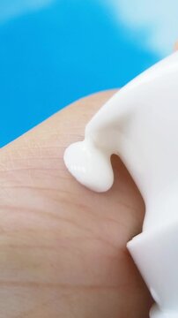 Pouring white cream onto hand skin. Cream slowly coming out from tip of cap. Close up view, moisturizing texture for daily skincare.