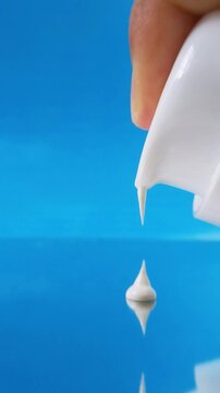White skin cream coming out from product packaging. White liquid on glass reflection with blue background. Close up texture for skincare concept.