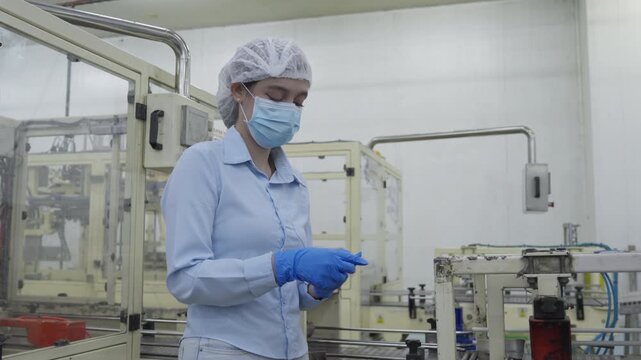 Food factory automated production line, Female worker in cleanroom wearing mask and gloves, examining hands near production machine in sterile factory production line, industrial quality control
