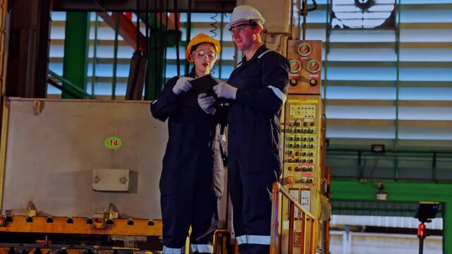 Industrial worker and technician in factory maintenance safety wearing helmet protective eyewear using tablet for inspection of machinery and production control panel teamwork on manufacturing floor
