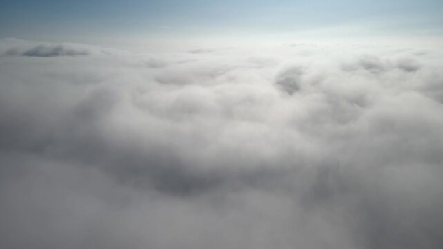 Aerial shot of flying over a layer of soft clouds at dawn