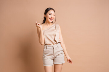 Obraz premium Happy Beautiful Young Asian Woman Pointing Fingers and Looking Away with Shy Excited Smile Portrait of Cheerful Girl in Beige Outfit Posing on Beige Background