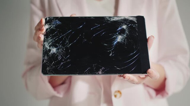 Person holding broken tablet computer with cracked screen displaying damage.