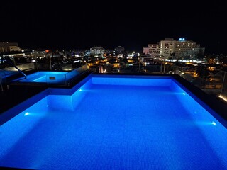 Fototapeta premium Rooftop pool glows under night sky with city lights in the background