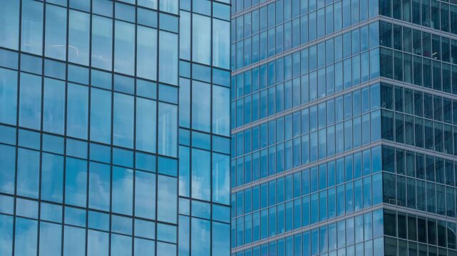 Close up timelapse of skyscraper glass facade reflecting moving white clouds, blue sky mirrored in windows, modern architecture texture and urban design concept