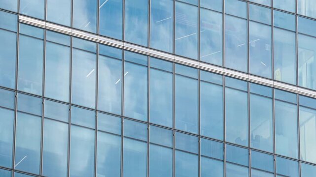 Close up timelapse of skyscraper glass facade reflecting moving white clouds, blue sky mirrored in windows, modern architecture texture and urban design concept