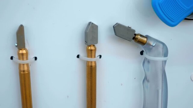 Samples of hand-held glass cutters hang on a white wall. Closeup. Follow focus