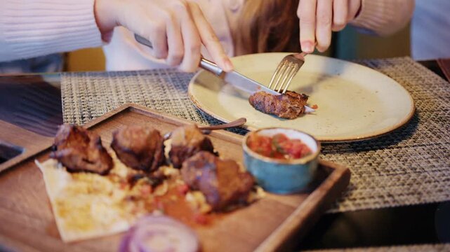 Close up of grilled pieces of meat placed on flatbread, while a person uses a knife and fork to cut into one piece