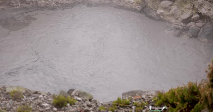 Volcanic pit with mud and boiling water with steam rising to the surface in a pond at Furnas, Azores.