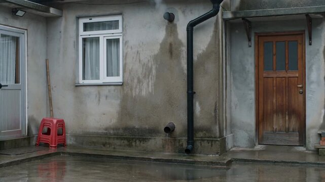 Rainwater Gently Cascading from a Gutter Downspout into a Wet Outdoor Courtyard, Illustrating Water
